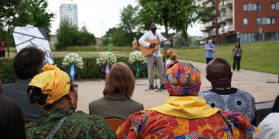Twe vrouwen in Surinaamse kleding kijken naar een man op een podium wie guitar speelt 