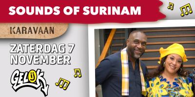 Een man en een vrouw kijken meteen glimlach naar de kamera. Ze dragen allebei kleurrijk Surinaamse accessoires